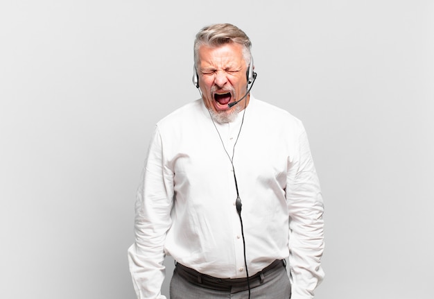 Operador de telemarketing sênior gritando agressivamente, parecendo muito zangado, frustrado, indignado ou irritado, gritando não