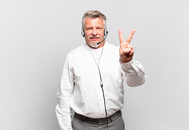 Operador de telemarketing sênior sorrindo e parecendo amigável, mostrando o número dois ou o segundo com a mão para a frente, em contagem regressiva