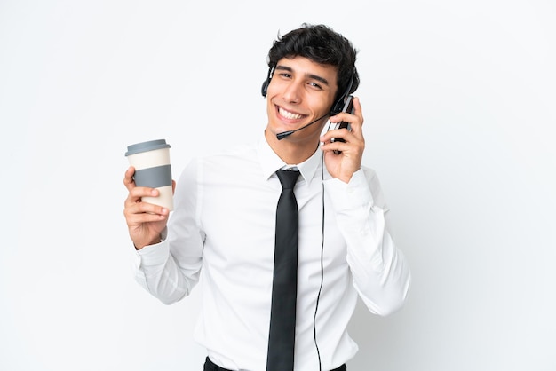 Operador de telemarketing trabalhando com um fone de ouvido isolado no fundo branco, segurando um café para levar e um celular