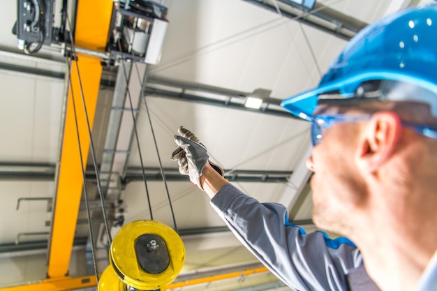 Foto operador de elevación de grúa montada en el techo del almacén explicando cómo funciona la máquina tecnologías industriales