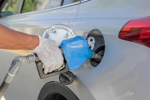 El operador de la estación de servicio sostiene una manguera de combustible para depositar gasolina en el vehículoxA