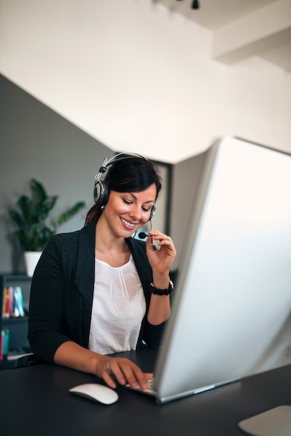 Operador fêmea de sorriso bonito que fala no auriculares com o cliente.