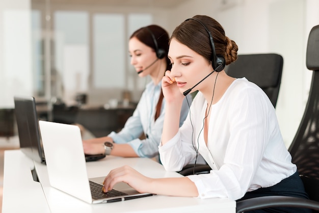 El operador femenino en el centro de llamadas responde a los clientes con auriculares y computadora portátil en la oficina de soporte técnico