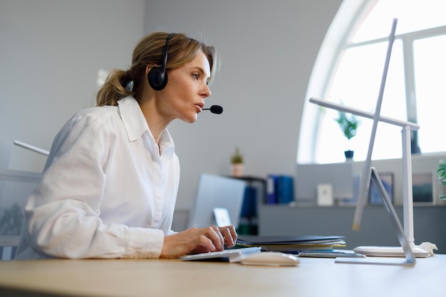 Operador de línea de ayuda de mujer de negocios en auriculares trabajando en la computadora