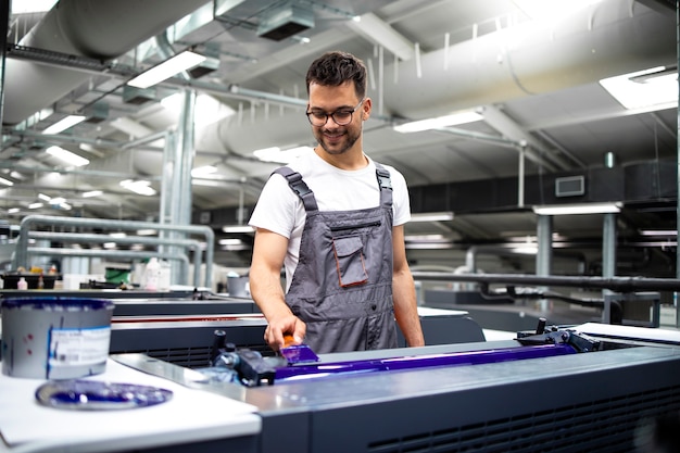 Operador de máquina de impresión profesional que agrega más color durante el proceso de impresión en la fábrica.