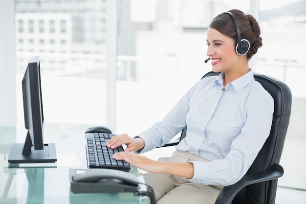 Operador de pelo castaño con clase alegre usando su computadora