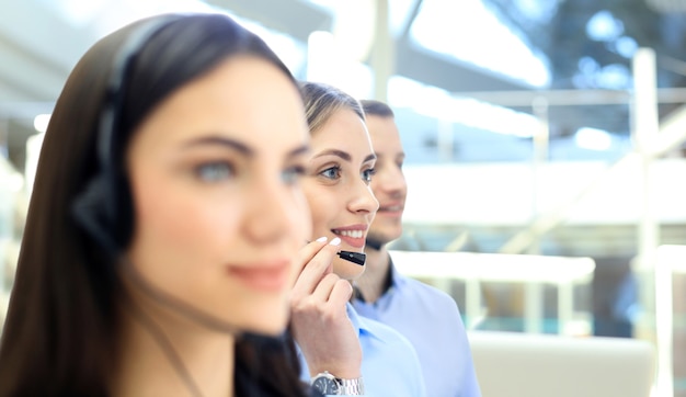 Operador de soporte al cliente femenino con auriculares y sonriendo, con colegas en segundo plano.