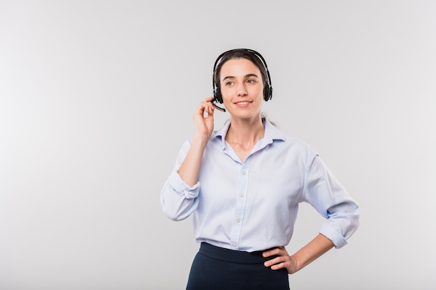 Operadora elegante, jovem e feliz com fone de ouvido, consultando clientes on-line enquanto fica parado na frente da câmera, isolado