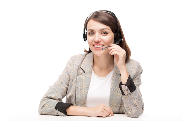 Operadora de línea directa femenina amigable joven del centro de llamadas que lo mira mientras consulta a uno de los clientes en línea
