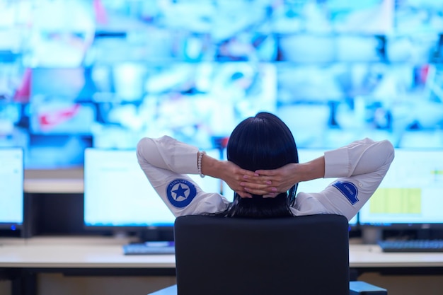 Operadora de seguridad femenina que trabaja en las oficinas de la sala de control de un sistema de datos Operadora técnica que trabaja en una estación de trabajo con varias pantallas, guardia de seguridad que trabaja en varios monitores