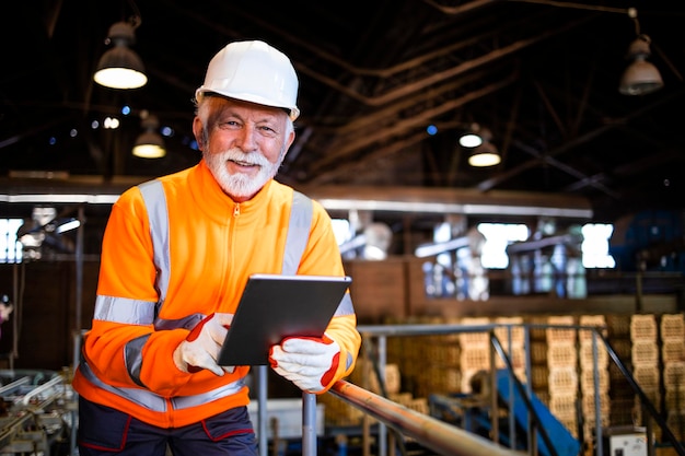 Operário de fábrica aguardando máquinas de produção e verificando os resultados de fabricação no computador tablet