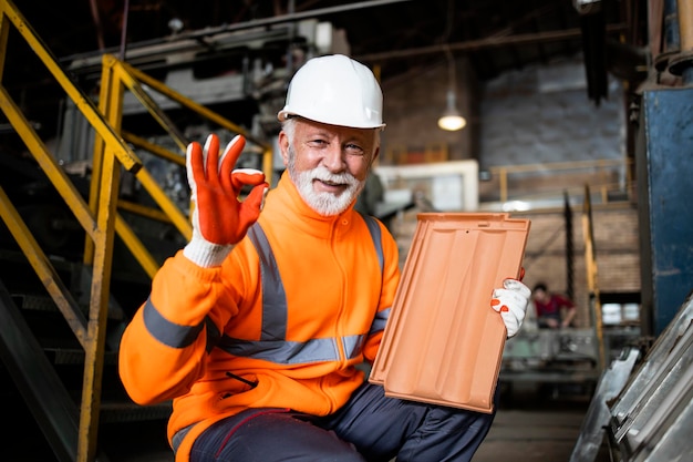 Operário de fábrica em equipamentos de segurança segurando o produto de telha de telha