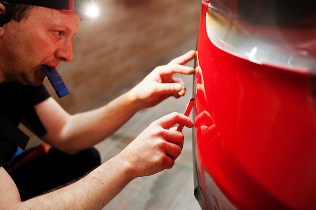 Foto operário de serviço automotivo colocou filme anti-cascalho em uma carroceria vermelha na oficina de detalhamento de veículos