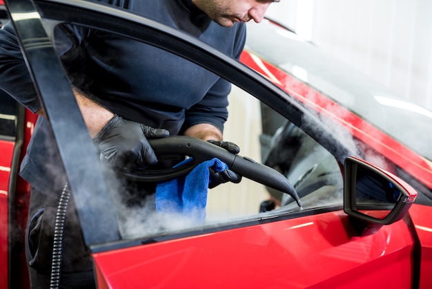 Operário de serviço automotivo limpa o interior com limpador a vapor