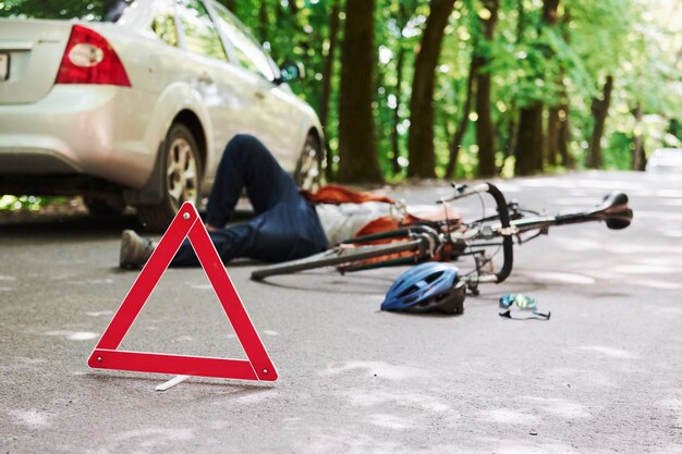 Opfer auf dem Asphalt. Fahrrad und silberfarbener Autounfall auf der Straße am Wald während des Tages