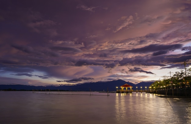 Opinião da paisagem do por do sol no lago com fundo colorido do céu da nuvem de tempestade.