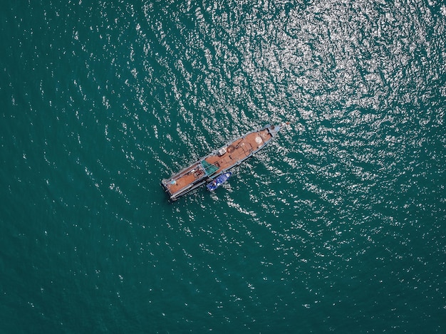 Opinião do zangão da lancha azul velha grande com plataforma vazia enorme no mar azul, bote salva-vidas violeta ao seu lado; conceito de navios.