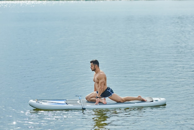 Opinião lateral o homem do ajuste que faz esticando os exercícios que sentam-se na placa do sup.