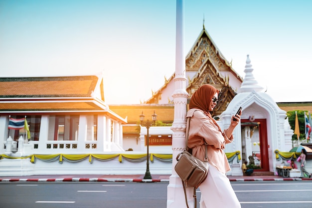 Opinião traseira o turista muçulmano da mulher que anda no templo de buddha, mulher asiática que usa o telefone celular na estrada. conceito de viagens.