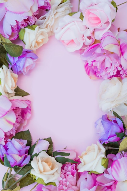 Opinión de alto ángulo de las flores artificiales coloridas que forman el marco en fondo rosado
