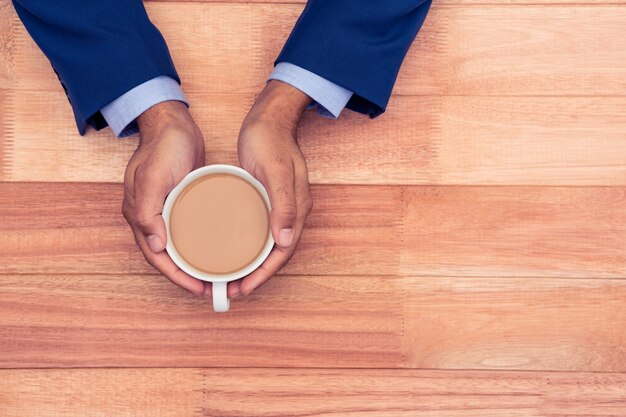 Opinión de alto ángulo el hombre de negocios que sostiene la taza de café en la tabla de madera