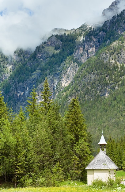 Opinión de la capilla vieja del pueblo de montaña de los dolomitas italianos del verano tranquilo.