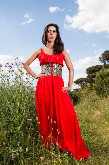 Opinión una mujer joven en un vestido rojo que presenta en naturaleza.