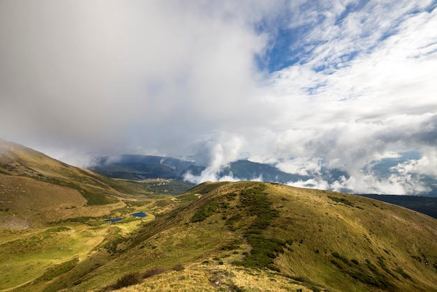 La opinión panorámica de las montañas verdes sobre el cielo azul con las nubes blancas copia el fondo del espacio en día soleado brillante. Concepto de turismo y viaje.