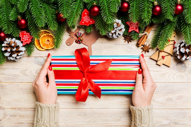 Opinión superior una mujer que sostiene una caja de regalo en sus manos en la tabla de madera festiva. Abeto y decadencias navideñas. Concepto de tiempo de año nuevo