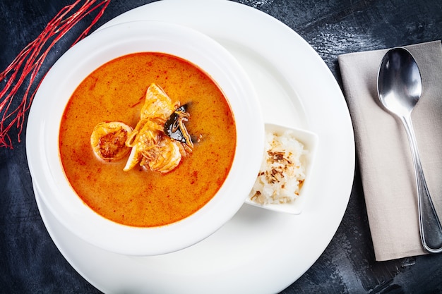 Opinión superior sobre la sopa de tom yum servida en la placa blanca con arroz. Sopa con camarones, mariscos, leche de coco y ají en un tazón copia espacio. Cocina tradicional de Tailandia. Almuerzo comida con espacio de copia