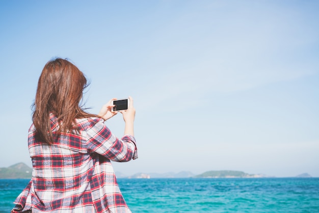 Foto opinión trasera una mujer que toma la fotografía con una cámara elegante del teléfono en el horizonte en la playa.