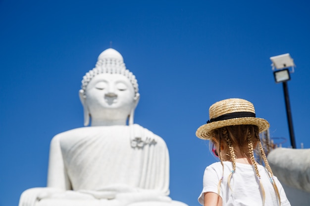 Opinión trasera la niña que se coloca cerca de la estatua grande de Buda en Phuket, Tailandia.