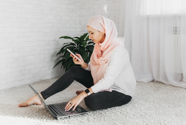 Oportunidades de trabalho para o conceito de mulheres muçulmanas. Menina sorridente em hijab falando ao telefone sentado no chão em casa.