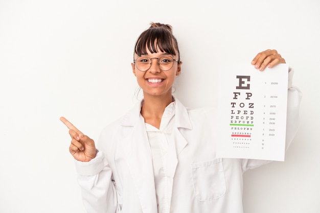 Óptico jovem de raça mista, fazendo um teste isolado no fundo branco, sorrindo e apontando para o lado, mostrando algo no espaço em branco.