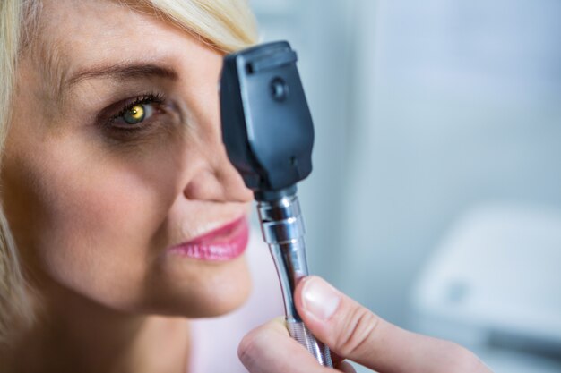 Optiker, der Patientin durch Ophthalmoskop untersucht