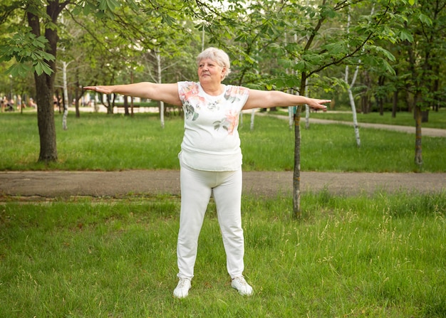 Optimistische alte Frau, die für gesundes Leben im Freien trainiert. Reife Frau, die Yoga praktiziert.