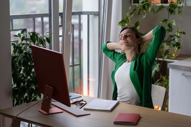 Optimistische Geschäftsfrau, die nach Abschluss eines schwierigen Projekts die Hand nach oben streckt, sitzt am Bürotisch