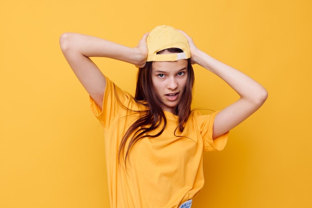 Optimistische junge Frau, die in einem gelben T-Shirt und in einem gelben Hintergrund der Kappe aufwirft