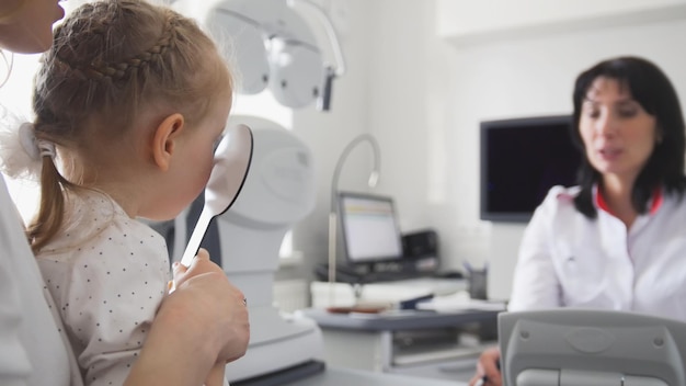 Optometrist in der Klinik, die das Sehen des kleinen Kindes überprüft - blondes kleines Mädchen schließt ein Auge, Weitwinkel