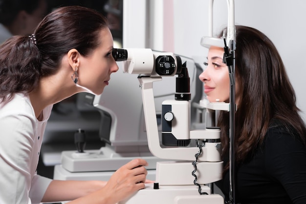 Optometrista atento examinando bela paciente do sexo feminino com lâmpada de fenda na clínica de oftalmologia Optometrista durante um exame em uma clínica moderna Verificação da visão Vista lateral