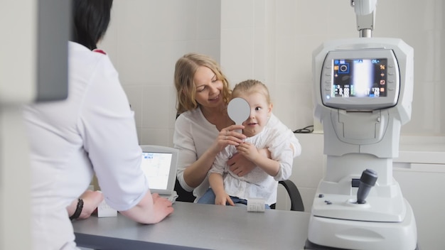 Optometrista comprueba la vista del niño: madre e hijo en la sala del oftalmólogo, horizontal