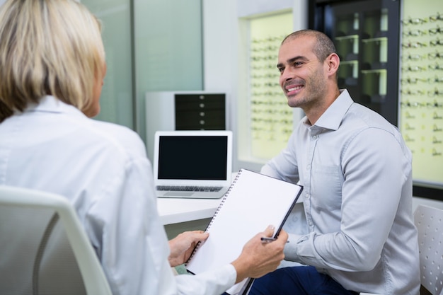 Optometrista femenino hablando con paciente masculino