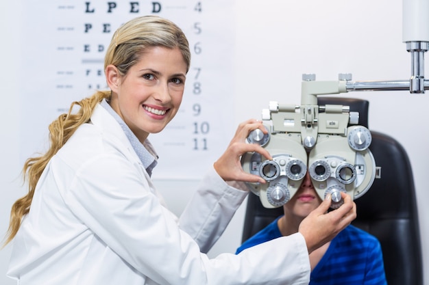 Optometrista femenino que examina al paciente joven en foróptero