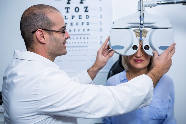 Optometrista sorridente, examinando o paciente do sexo feminino em phoropter