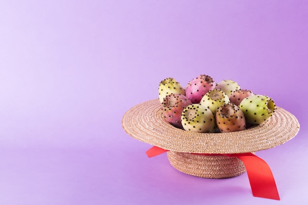 Opuntia fruta en un sombrero de paja sobre un fondo morado de moda