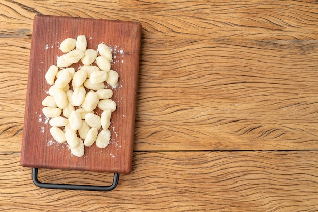 Ñoquis de pasta italiana sin cocer en un tablero sobre una mesa de madera con espacio para copiar