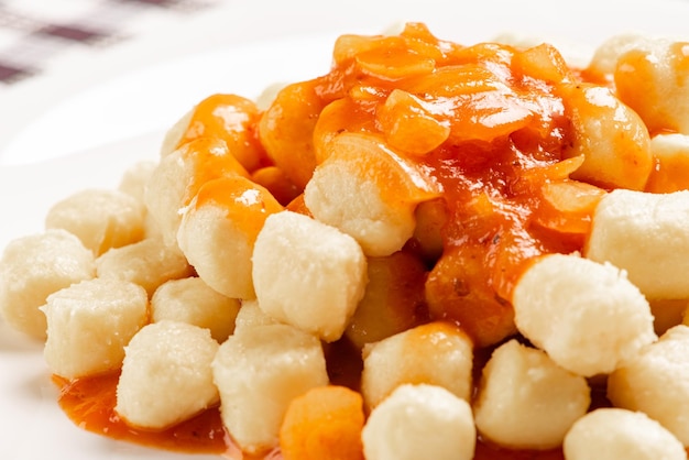 Ñoquis de patata con salsa en detalle sobre un plato blanco sobre un mantel a cuadros blanco y negro, enfoque selectivo.