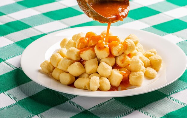 Ñoquis de patata con salsa en detalle sobre un plato blanco sobre un mantel a cuadros verde y blanco, enfoque selectivo.