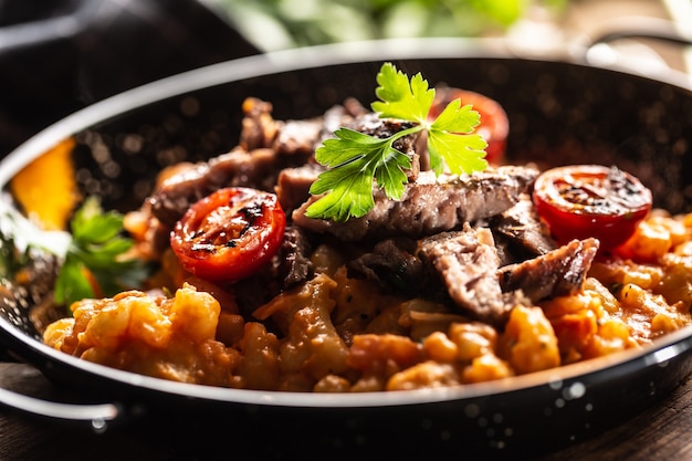 Ñoquis de salsa de tomate con ternera sous-vide y tomates frescos servidos en un plato oscuro.