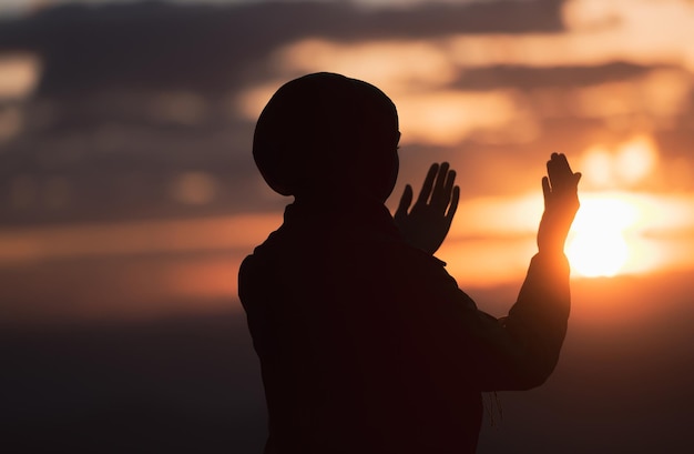 Oração da mulher muçulmana tendo adoração e orando com as mãos abertas fazendo dua para Allah ao pôr do sol